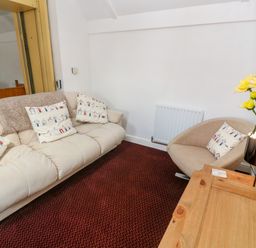 A sitting area with a beige sofa and armchair with patterned cushions and a wooden table with yellow flowers at The Stables in Longrock
