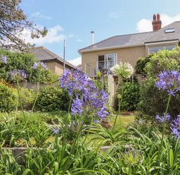 A garden with purple and white flowers and a house with a balcony in the background at Sunset in St Just