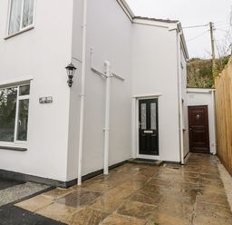 The exterior side of a white building with two doors a wooden fence and paved ground at Avalon in St Agnes
