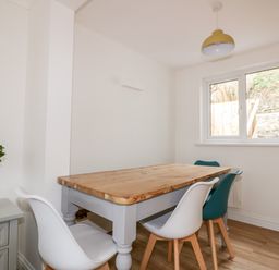 A dining area with wooden table four chairs and a small plant on a cabinet by a window at Avalon in St Agnes
