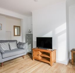 A living room with a grey sofa a wooden TV stand with a television a wooden side table and a chest of drawers at Avalon in St Agnes