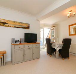 A dining area with a table and four chairs next to a sideboard with a television and stereo at Seashore in Woolacombe