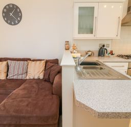 A brown sofa with cushions and a kitchen counter with a sink kettle and stove at Seashore in Woolacombe