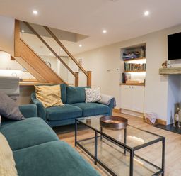 A living room with teal sofas coffee table bookshelf and wood burning stove at St Marys Cottage in Windermere