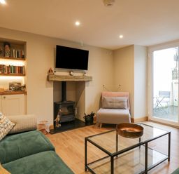 A living room with a green sofa a glass coffee table and a wood burning stove at St Mary's Cottage in Windermere