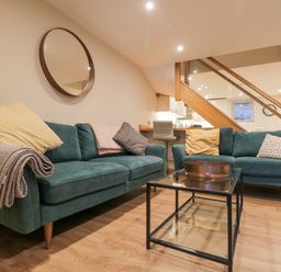 A living room with two green sofas and a glass coffee table under wooden stairs at St Marys Cottage in Windermere