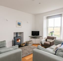 A living room with sofas a armchair a TV and a wood burning stove at The Upper Deck in Porthcurno