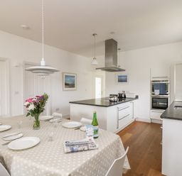A kitchen with a dining table set with plates glasses and cutlery and a bouquet of flowers on a table at The Upper Deck in Porthcurno