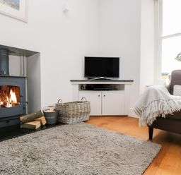 A living room with a wood burning stove television basket with firewood and a sofa with a throw at The Upper Deck in Porthcurno