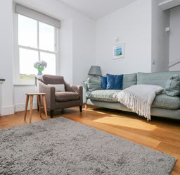 A living room with a sofa and armchair by a window and a gray rug on a wood floor at The Upper Deck in Porthcurno
