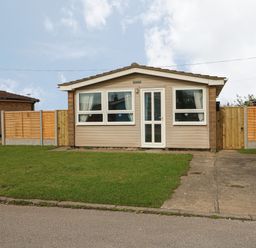 A small single-story house with a front lawn driveway and wooden fences at Moggs Retreat in Chapel St Leonards