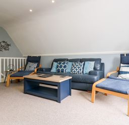 A living room with a blue leather sofa two blue armchairs a blue coffee table and a metal fish wall decoration at Valley Lodge 52 in Callington