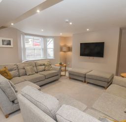 A living room with gray sofas, a wall-mounted TV, two ottomans, side tables with lamps, and a bay window at Station House in Scarborough