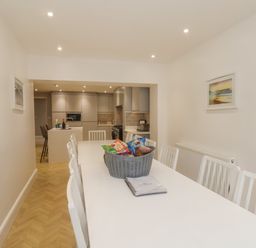 A dining room with white table and chairs leading to a kitchen with grey cabinets at Station House in Scarborough