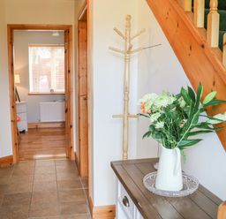 An entryway with a wooden coat rack a vase with flowers on a table and stairs with wooden handrail at The Blue Annex The Spa near Tralee County Kerry