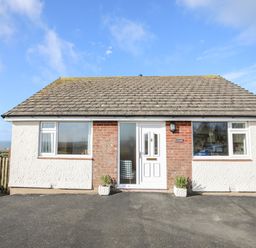 A single story house with white walls and a tiled roof with a paved driveway at Yr Orsedd in Llanfaethlu