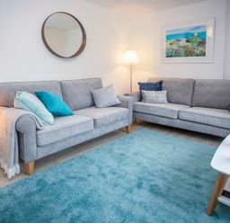 A living room with two grey sofas a blue rug a round mirror and a floor lamp at Bryn Teg Cottage in Menai Bridge