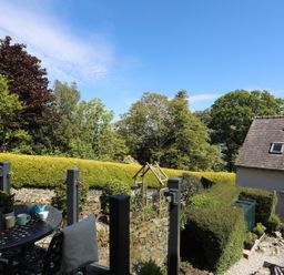 An outdoor patio with a round metal table and chairs overlooking a garden with hedges and trees at Bryn Teg Cottage in Menai Bridge