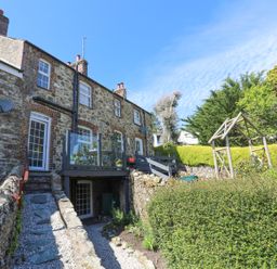 Stone house with balcony and garden area with wooden structure and trimmed hedges at Bryn Teg Cottage in Menai Bridge