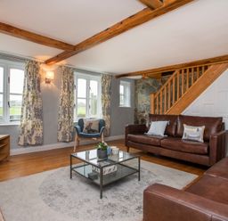 A living room with leather sofas a glass coffee table a blue armchair and a television at Stabl Bach in Llanfaethlu