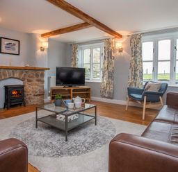 A living room with a stone fireplace television armchair coffee table and floral curtains at Stabl Bach in Llanfaethlu