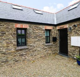 Stony courtyard with two small windows a black door and a potted plant at The Old Stables in Fishguard