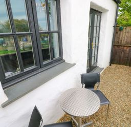 An outdoor patio area with a small round metal table and two black chairs beside white walls and black-framed windows at The Old Stables in Fishguard