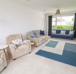 A living room with beige armchairs blue sofa and blue patterned rug at Seacoast Cottage in Castlerock