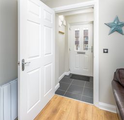 A hallway with a white door leading outside a brown leather sofa and blue star wall decoration at 39 Longbeach Drive in Beadnell