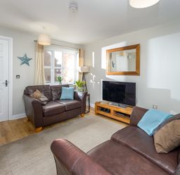 A living room with two brown leather sofas a television on a wooden stand and a wall mirror at 39 Longbeach Drive in Beadnell
