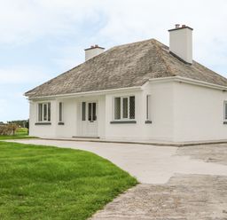 A detached white house with a sloped roof two chimneys a concrete driveway and green lawn at Dirreen House in Athea near Listowel County Kerry