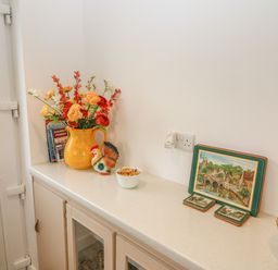 A kitchen countertop with a yellow jug of flowers a ceramic rooster figurine a bowl of wrapped candies books and a set of coasters at Dirreen House Athea near Listowel County Kerry