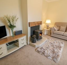A living room with a beige sofa a wood stove and a TV on a cabinet at Dirreen House in Athea near Listowel County Kerry