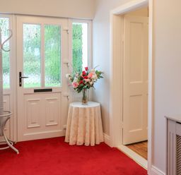 An entryway with a white door a white coat rack a small round table with a flower arrangement and red carpet at Dirreen House in Athea near Listowel County Kerry