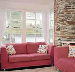 A living room with pink sofas and a television at Stargazy in Trebarwith Strand near Tintagel
