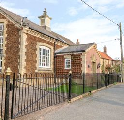 A street view of a stone building with large windows and a black metal fence at The Old School in Downham Market