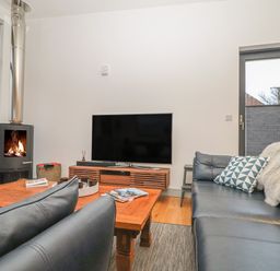 A living room with a black leather sofa a wooden coffee table a flat screen tv on a wooden stand and a wood burning stove at Idlewild 2 Wheal Turnavore in St Agnes