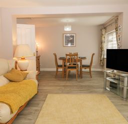 A living room with a sofa, lamp, dining table with chairs, television on a glass stand, and floral curtains at 2 The Close in Robin Hood'S Bay