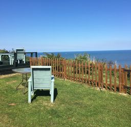 A grassy outdoor area with wooden chairs and tables near a wooden fence overlooking the sea at 2 The Close in Robin Hood'S Bay