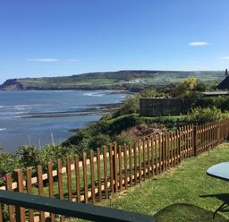 A fenced garden with a table and statue overlooking a bay and hillside at 2 The Close in Robin Hood'S Bay