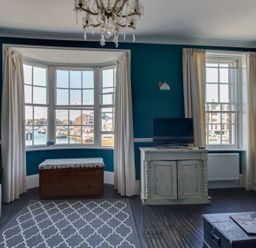A living room with a television on a cabinet a wooden chest under a bay window and a patterned rug on the floor at Sailor's Watch in Weymouth