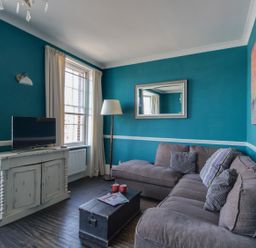 A living room with a gray sectional sofa a black trunk table a white cabinet with a TV and blue walls at Sailor's Watch in Weymouth