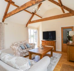 A living room with wooden beams sofas a coffee table a television and wooden furniture at Golden Valley Barn in Oldbury-On-Severn