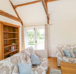 A sitting room with sofas a wooden bookshelf and glass doors leading outside at Golden Valley Barn in Oldbury-On-Severn