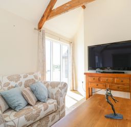 A living room with a floral patterned sofa with cushions a wooden table with a sculpture a wooden TV stand with a flat screen TV and large glass doors at Golden Valley Barn in Oldbury-On-Severn