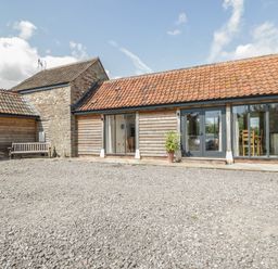 A gravel courtyard in front of a wooden building with glass doors and a tiled roof at Golden Valley Barn in Oldbury-On-Severn