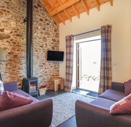 A living room with two sofas a wood stove and a television mounted on a stone wall at Y Bwthyn in Brynsiencyn