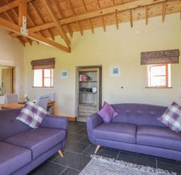 A living room with two purple sofas and a dining table with chairs at Y Bwthyn in Brynsiencyn