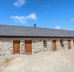 Exterior of a stone building with six wooden doors and two small windows with flower boxes at Y Bwthyn in Brynsiencyn