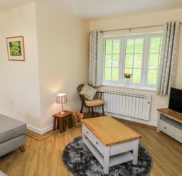 A living room with a gray sofa wooden coffee table round rug wooden chair and a television at Ryedale Country Lodges - Willow Lodge Kirkbymoorside